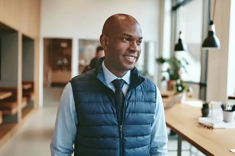 Smiling investor in a quilted vest and tie in an office