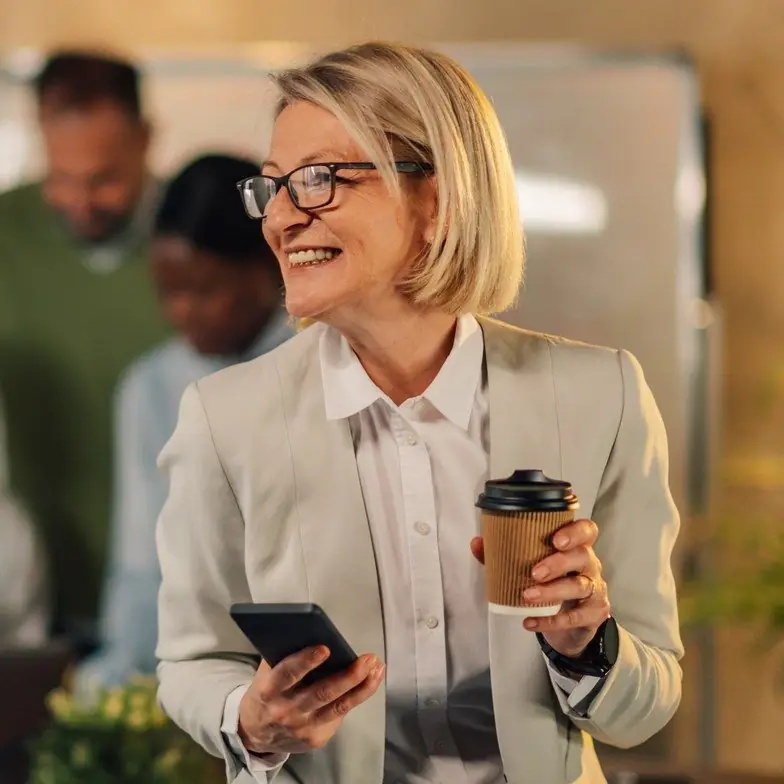 Smiling businesswoman with glasses holding a coffee and phone in a meeting