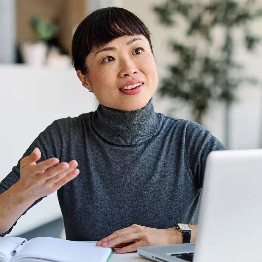 Executive in a grey turtleneck talking through plans at a laptop