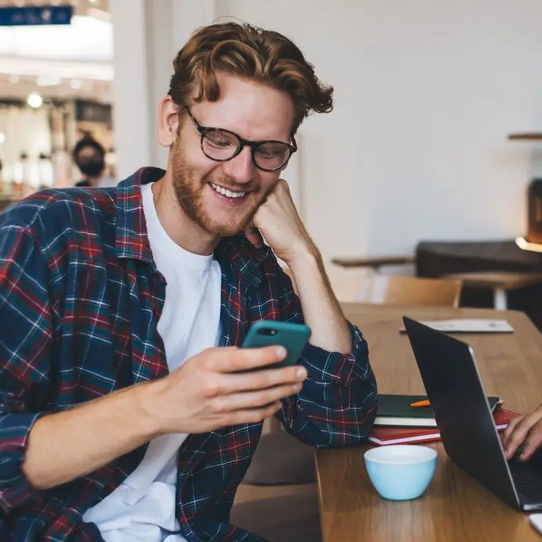 Smiling bearded man with glasses in a plaid shirt checking his phone at work