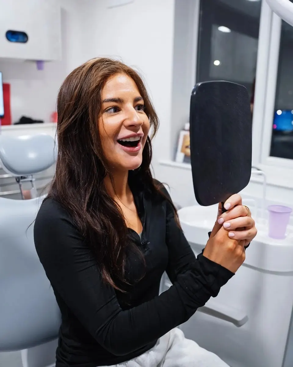 A patient laughing with joy as she sees her new smile in a hand mirror at Sale Dental Spa