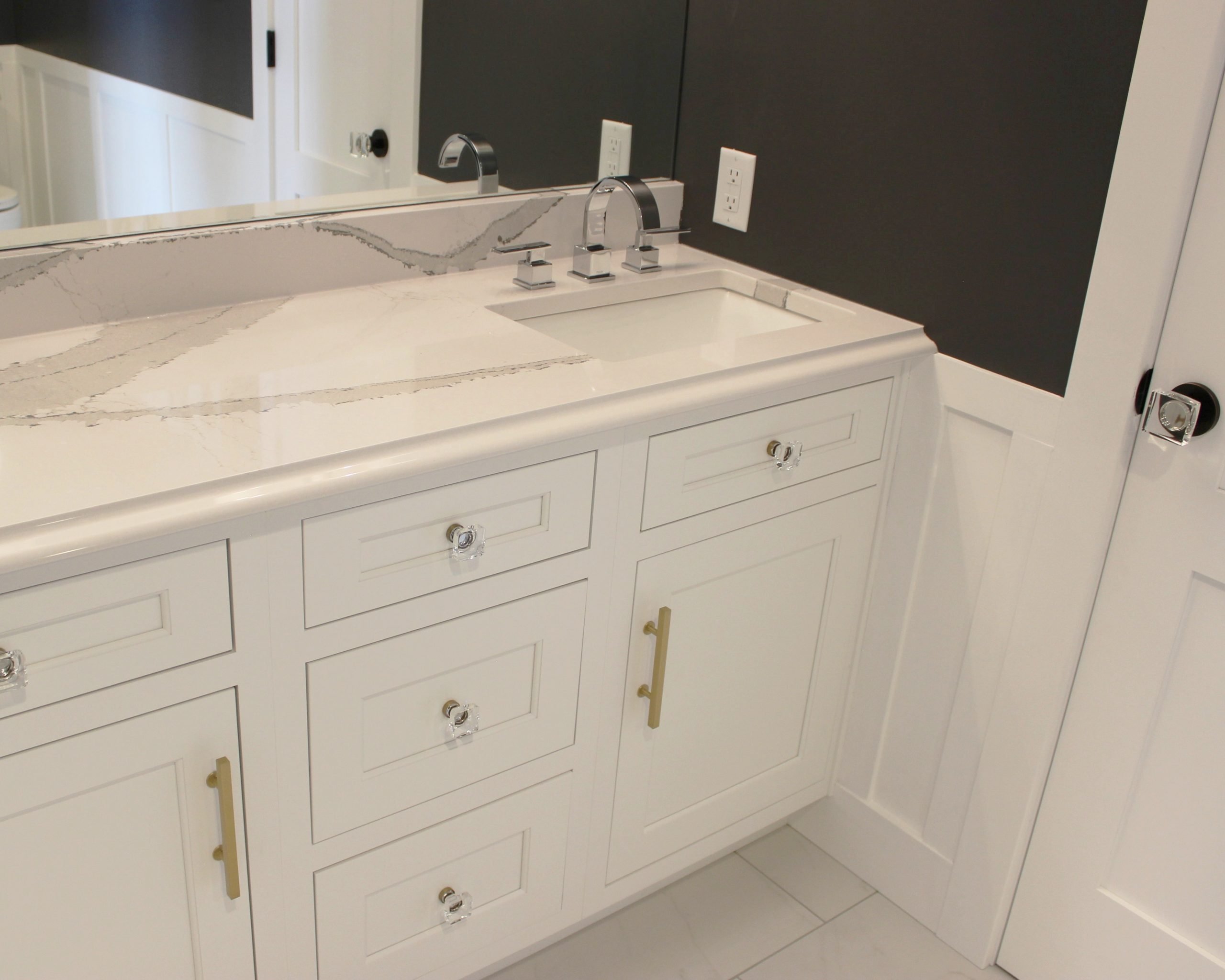 White bathroom vanity with a rectangular sink, chrome faucet, large mirror, and dark wall.