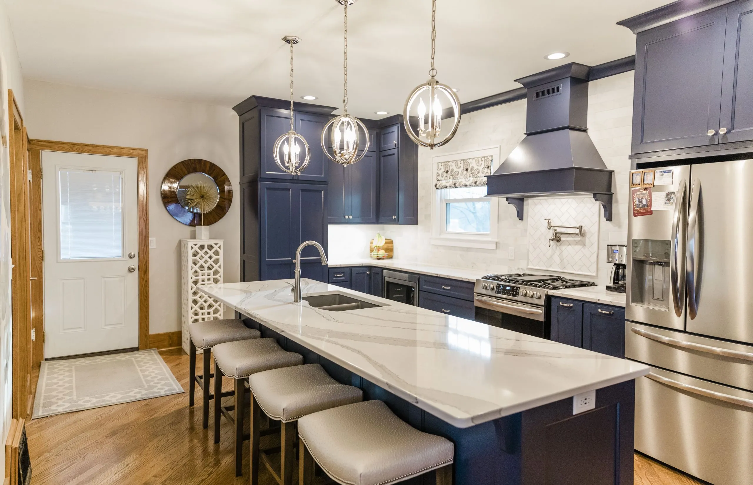 Kitchen with navy cabinets, a large white island, stainless appliances, and three pendant lights.