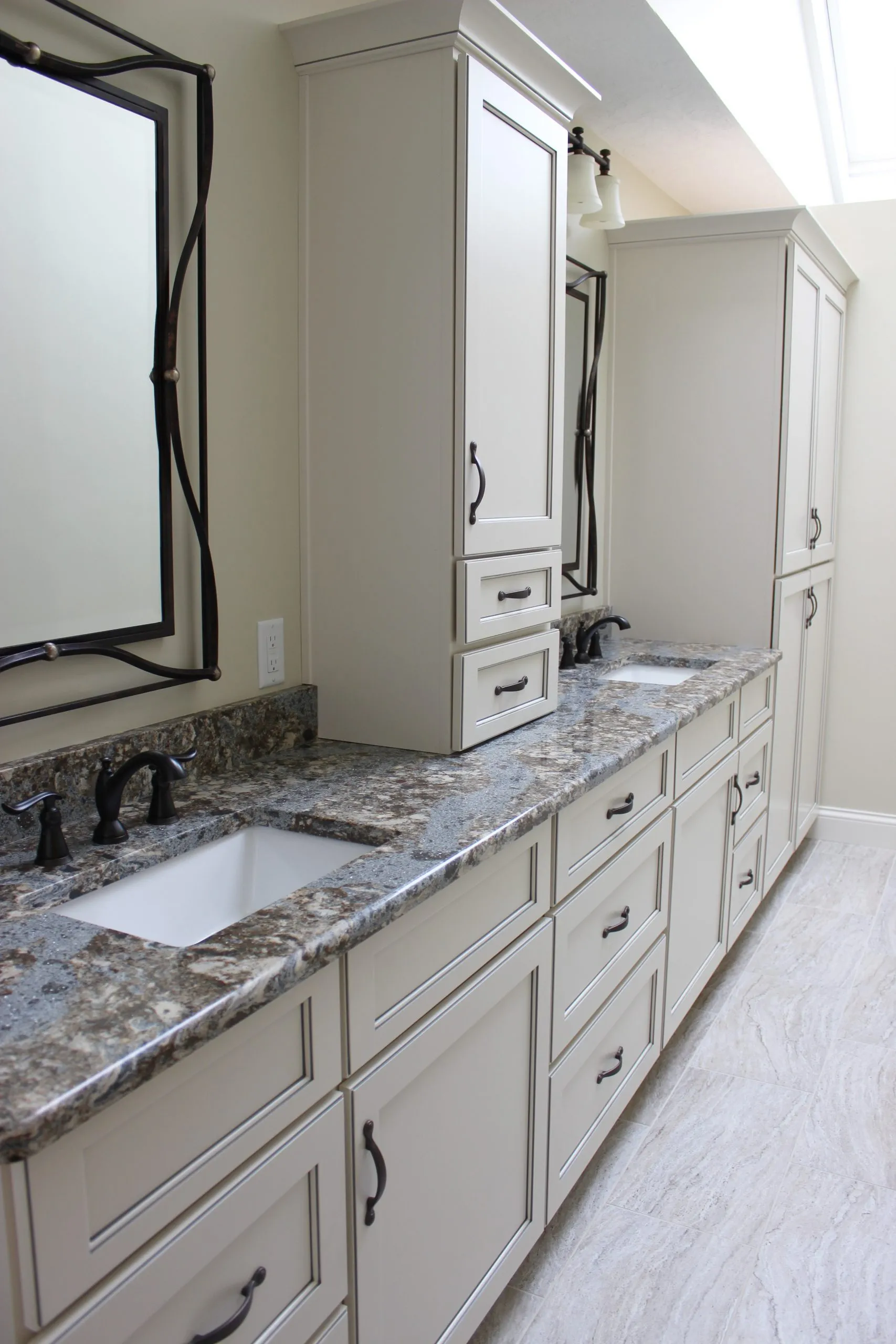 Bright bathroom vanity with cream cabinets, granite counters, framed mirrors, two sinks, and wall lights.