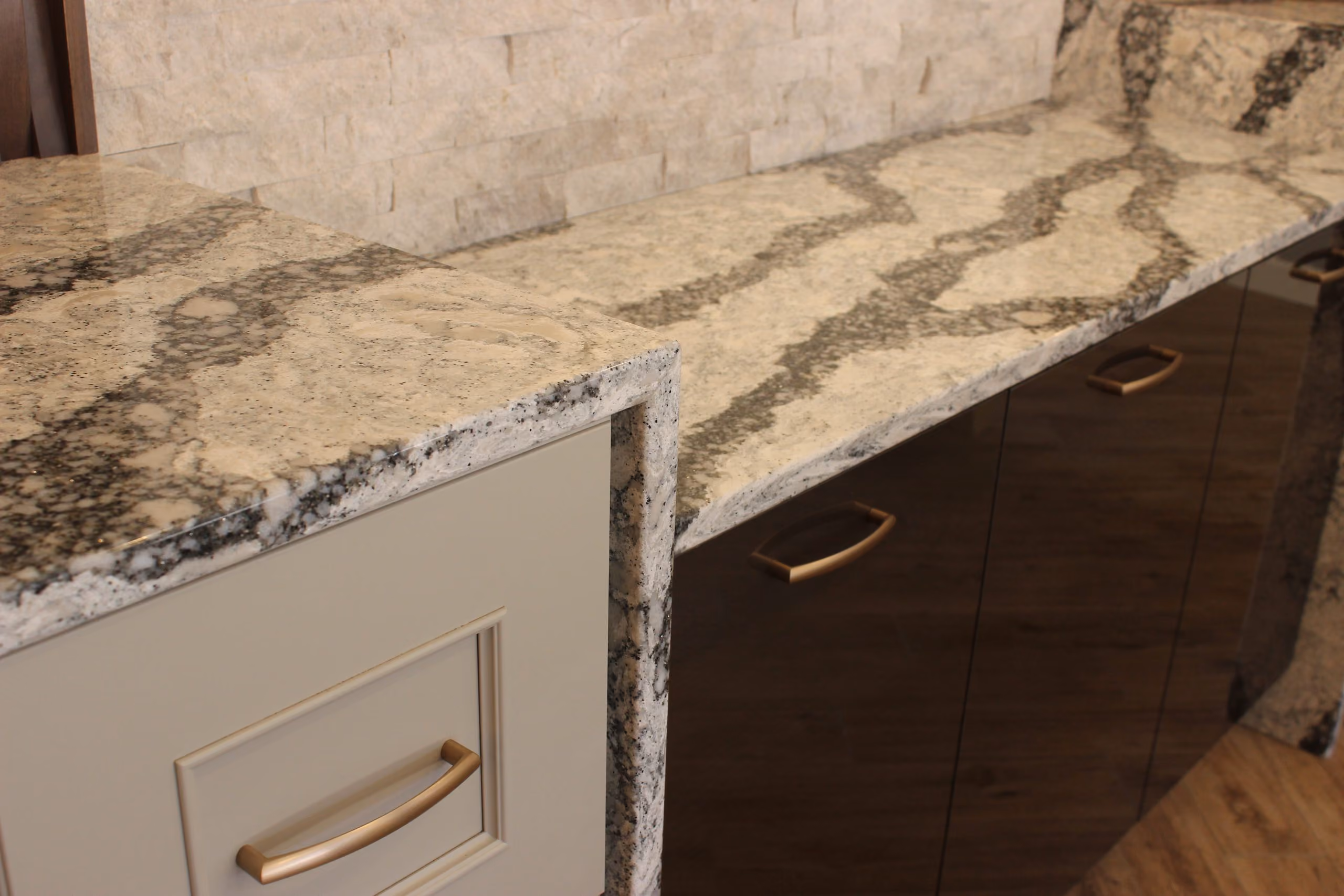 L-shaped stone kitchen countertops with white and dark wood cabinets and gold handles.