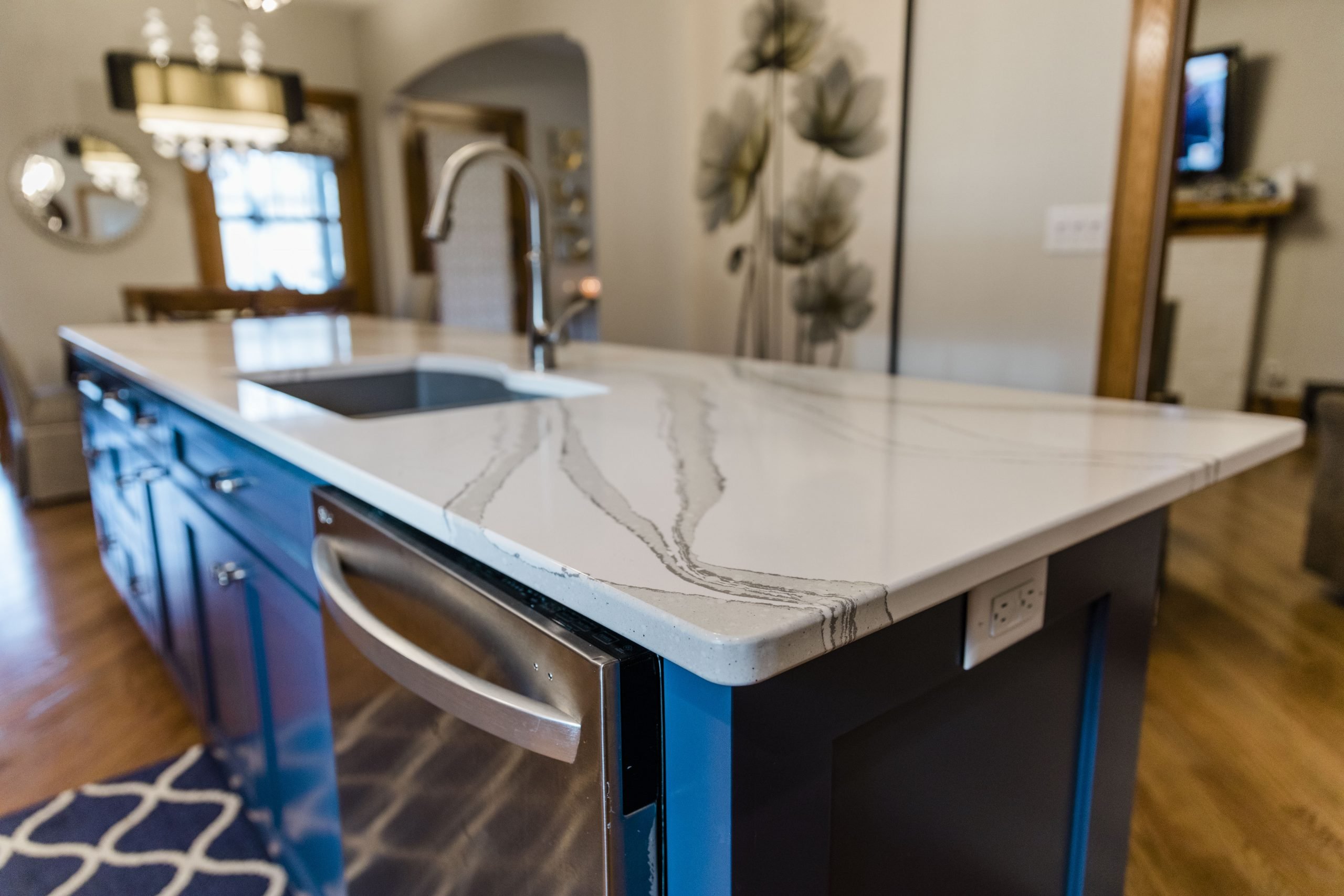 Kitchen island with a white marble-patterned countertop, blue cabinets, sink, and faucet.