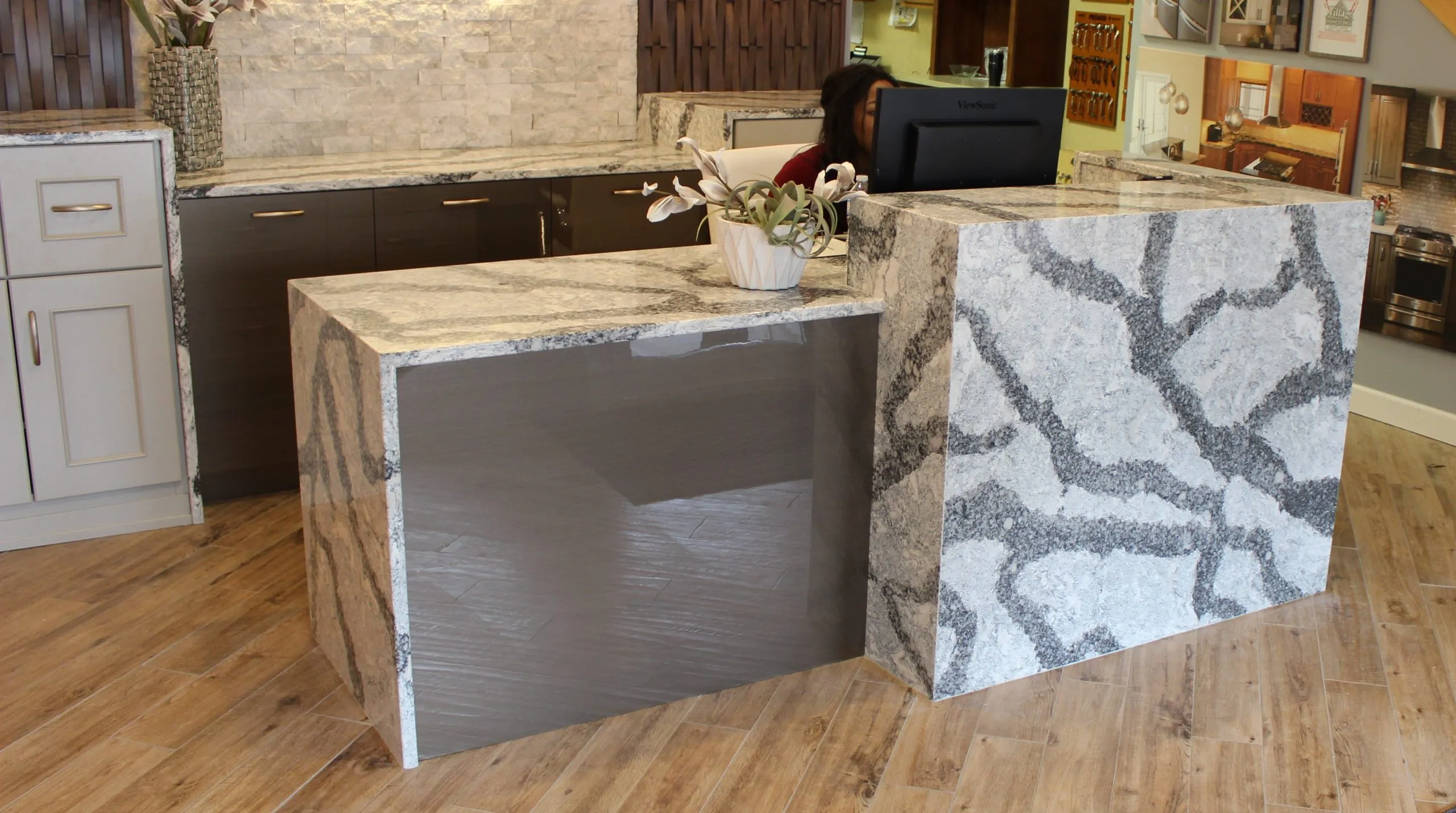 Modern showroom with marble counters, dark cabinetry, a flower arrangement, and a person behind a monitor.