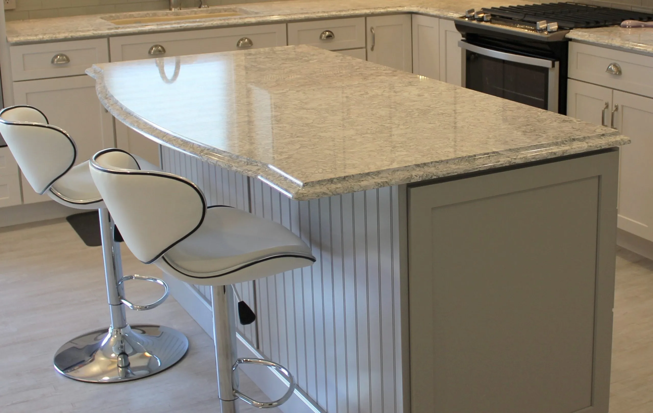 Modern kitchen with a large stone island, two white bar stools, white cabinets, and a black range.