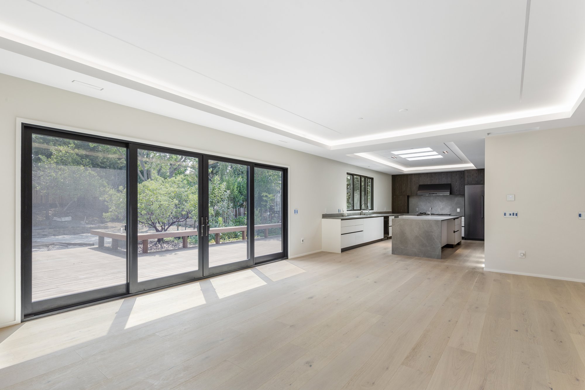 Open-plan kitchen and living area with a broad island, warm wood cabinetry, and sliding glass doors.