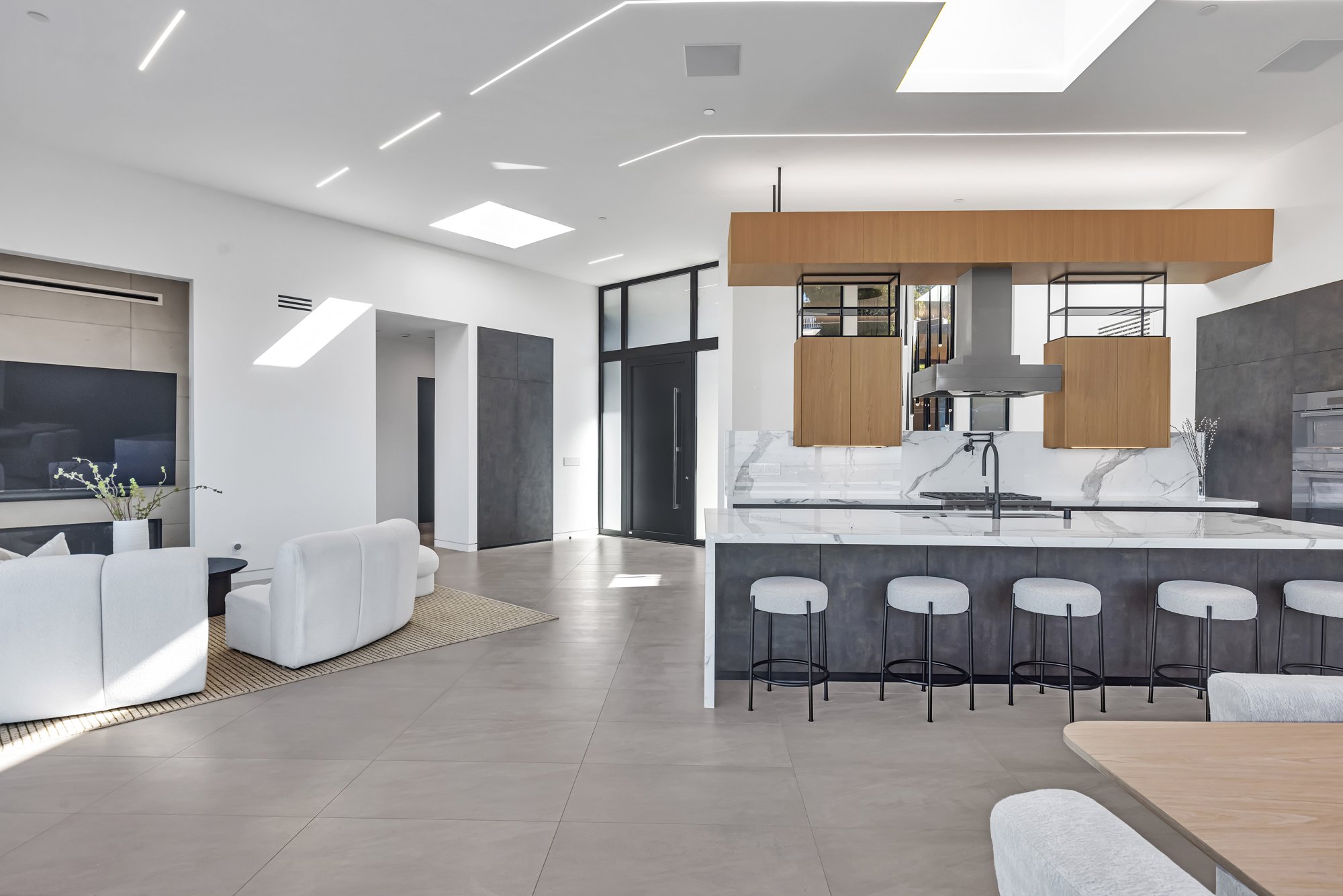 Open living and kitchen space with broad landscape glazing, skylights and pale cabinetry.