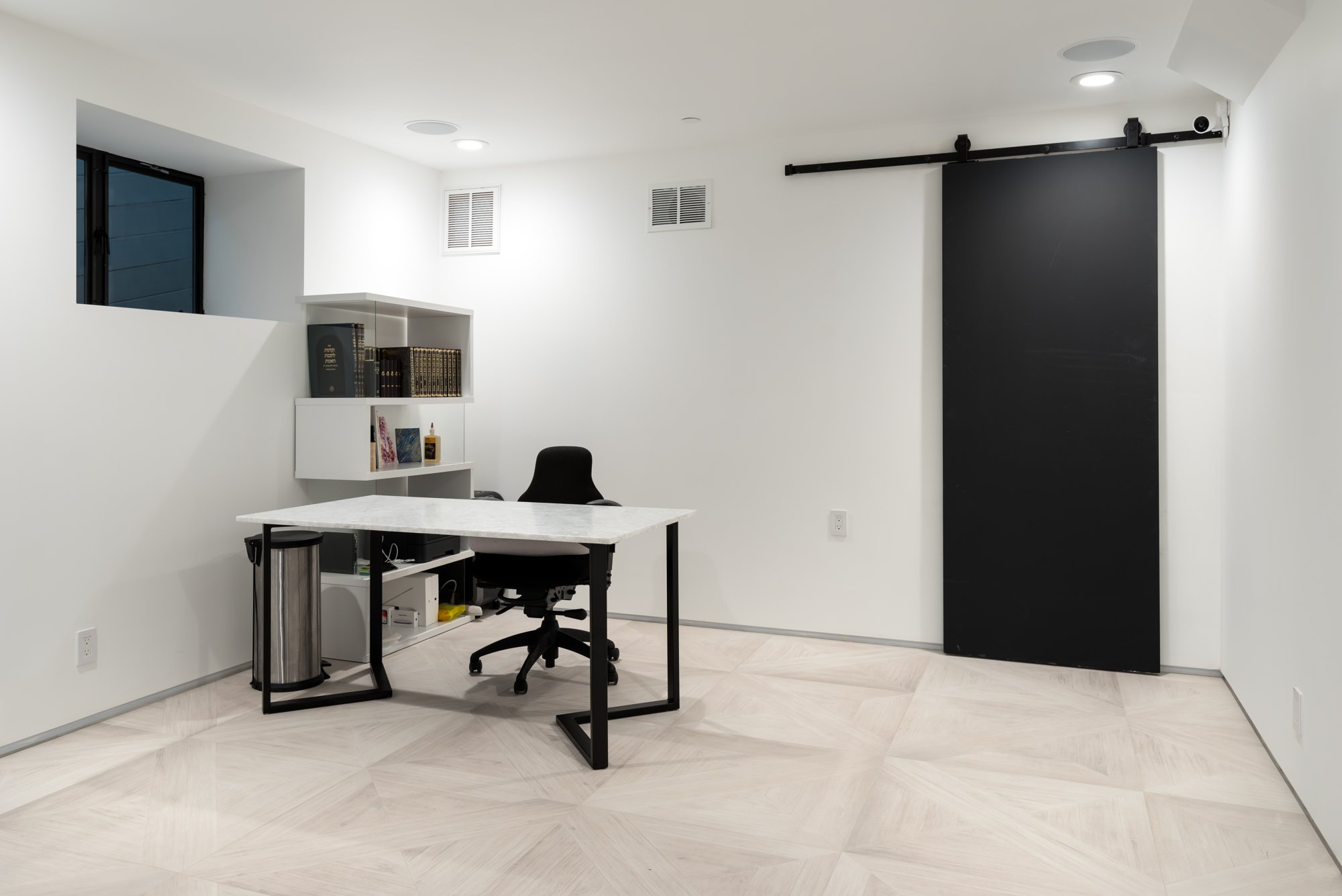 Home office with a central desk, black sliding door and tiled floor.