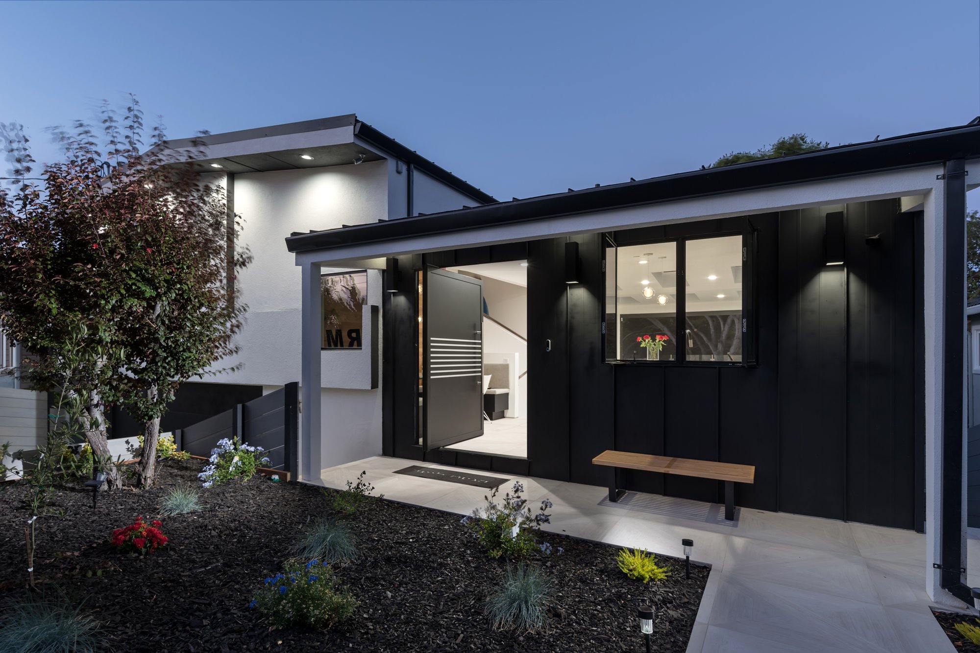 Contemporary home at dusk with illuminated interiors opening onto a planted terrace.