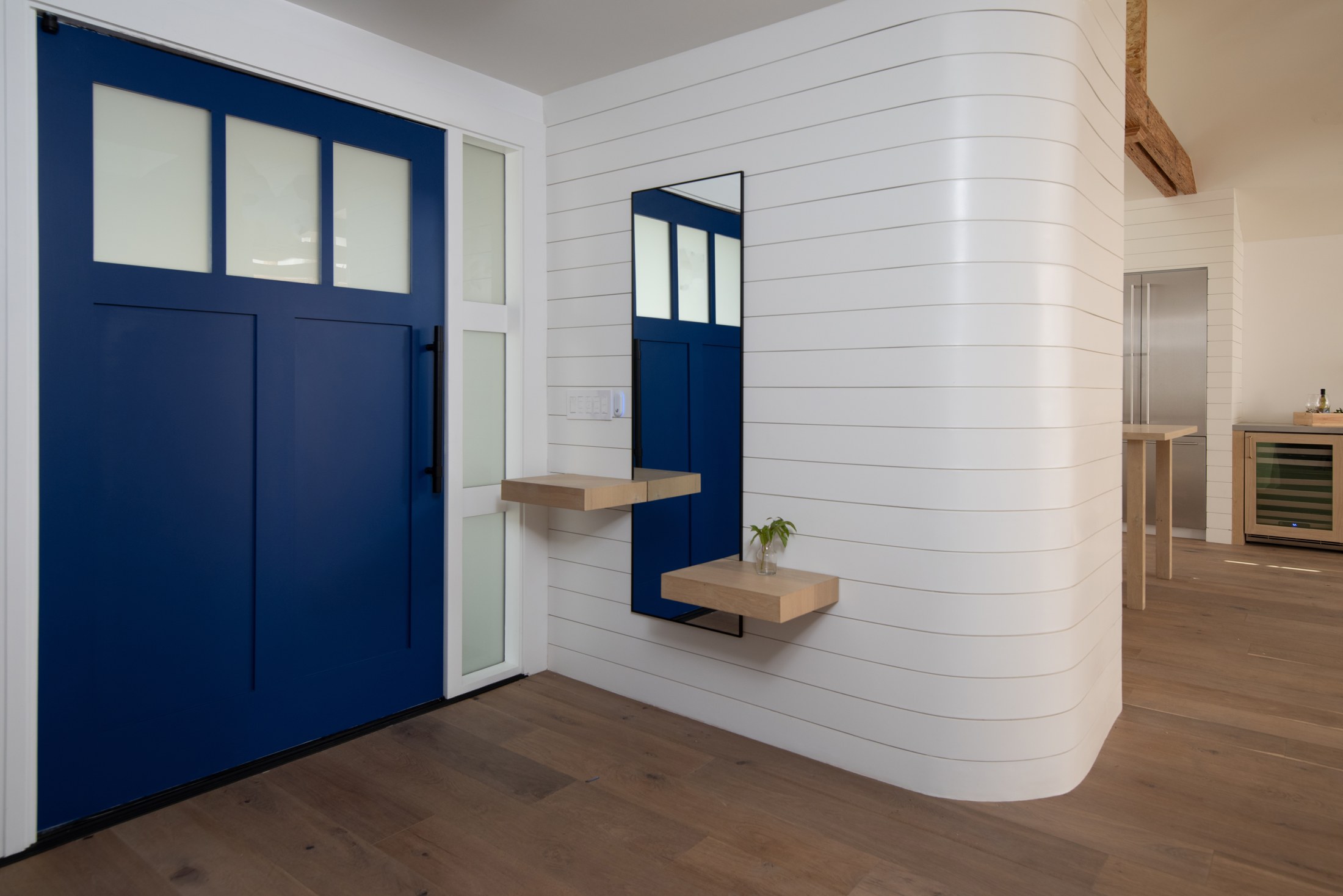 Entry with a blue door, curved white wall and a floating timber shelf.