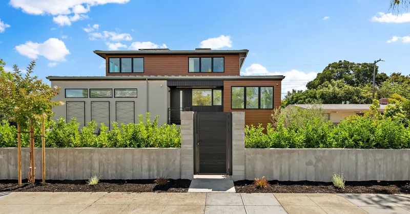 Modern house with layered rooflines, wood siding and a planted front approach.