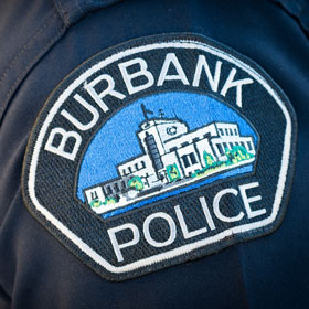 Patch on a police uniform sleeve with the words 'Burbank Police' surrounding an image of a white building with blue sky background.
