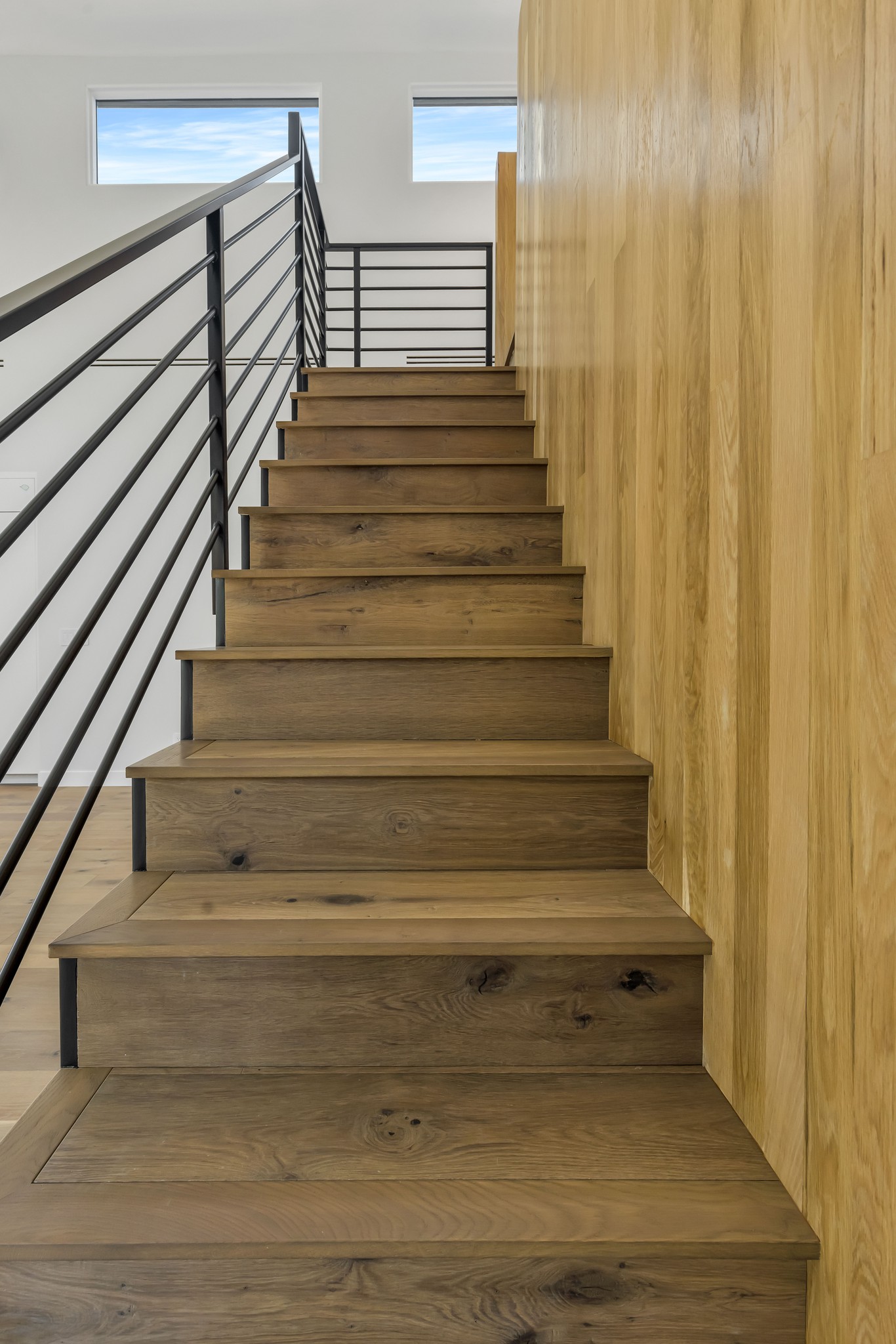 Wood staircase with horizontal metal railing and wood-paneled wall.