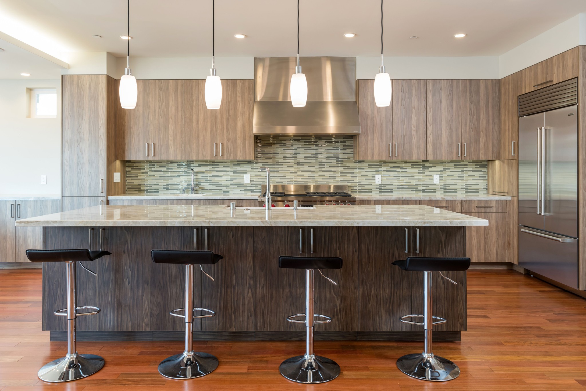 Kitchen island with four stools, pendant lights and wood cabinetry.