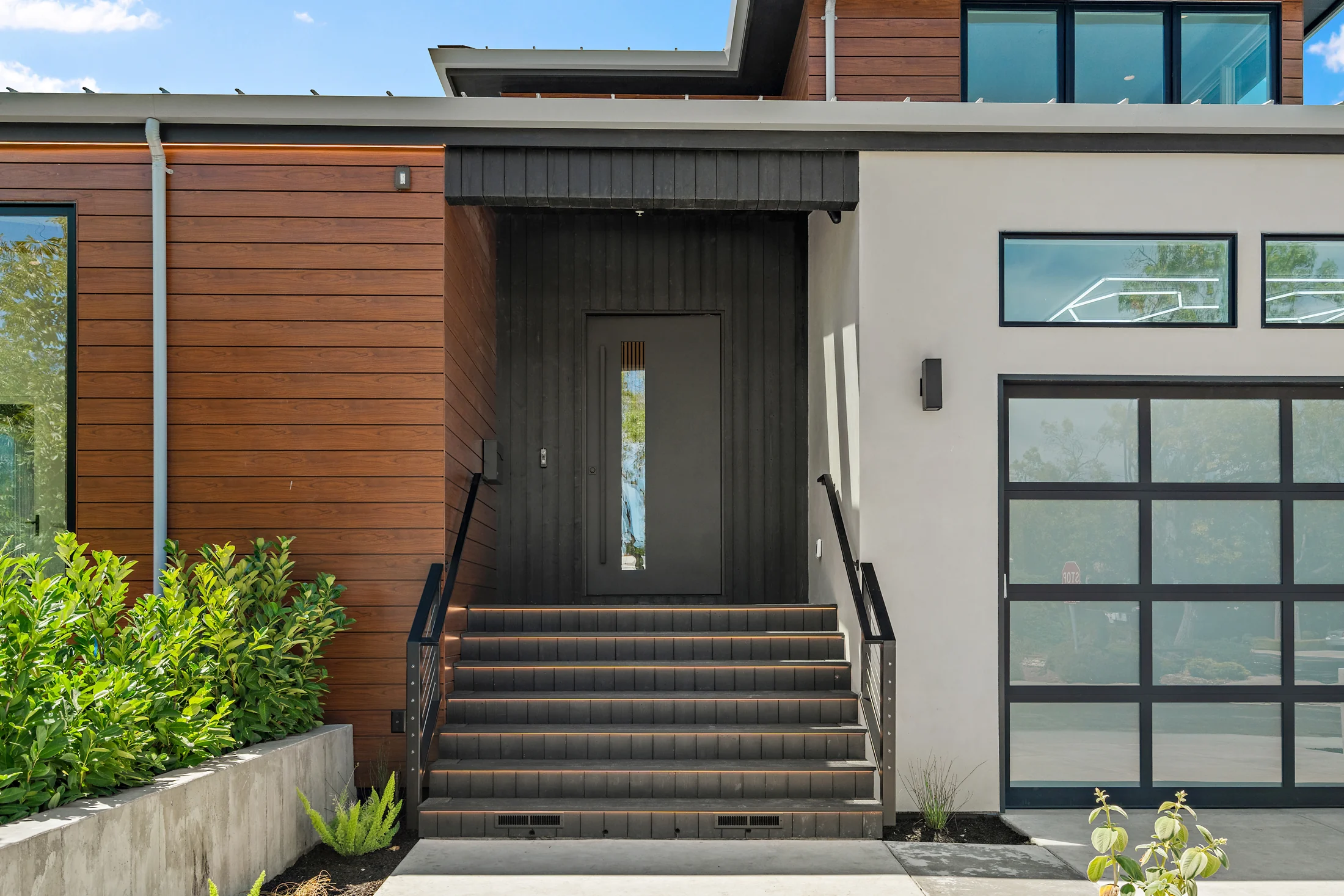 Recessed front door and tiled entry steps beside wood cladding and a glass-panel garage door.