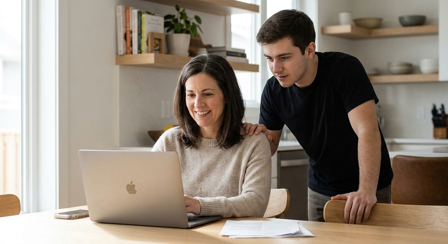 A smiling woman completes her ABLE disability verification on a laptop at home while her son looks on
