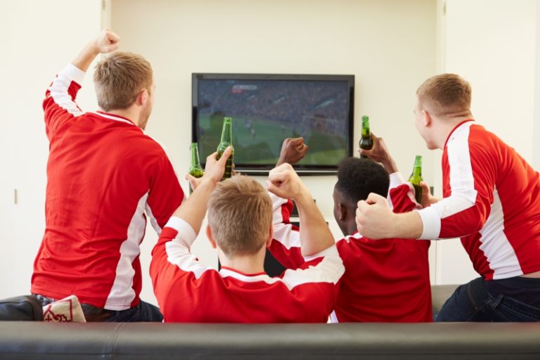 Friends in red jerseys cheering while watching a football game