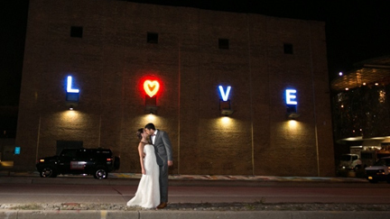 Couple embracing at night outside a wedding venue with a lit LOVE sign