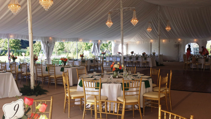 Tented wedding reception with chandeliers, round tables and gold chairs
