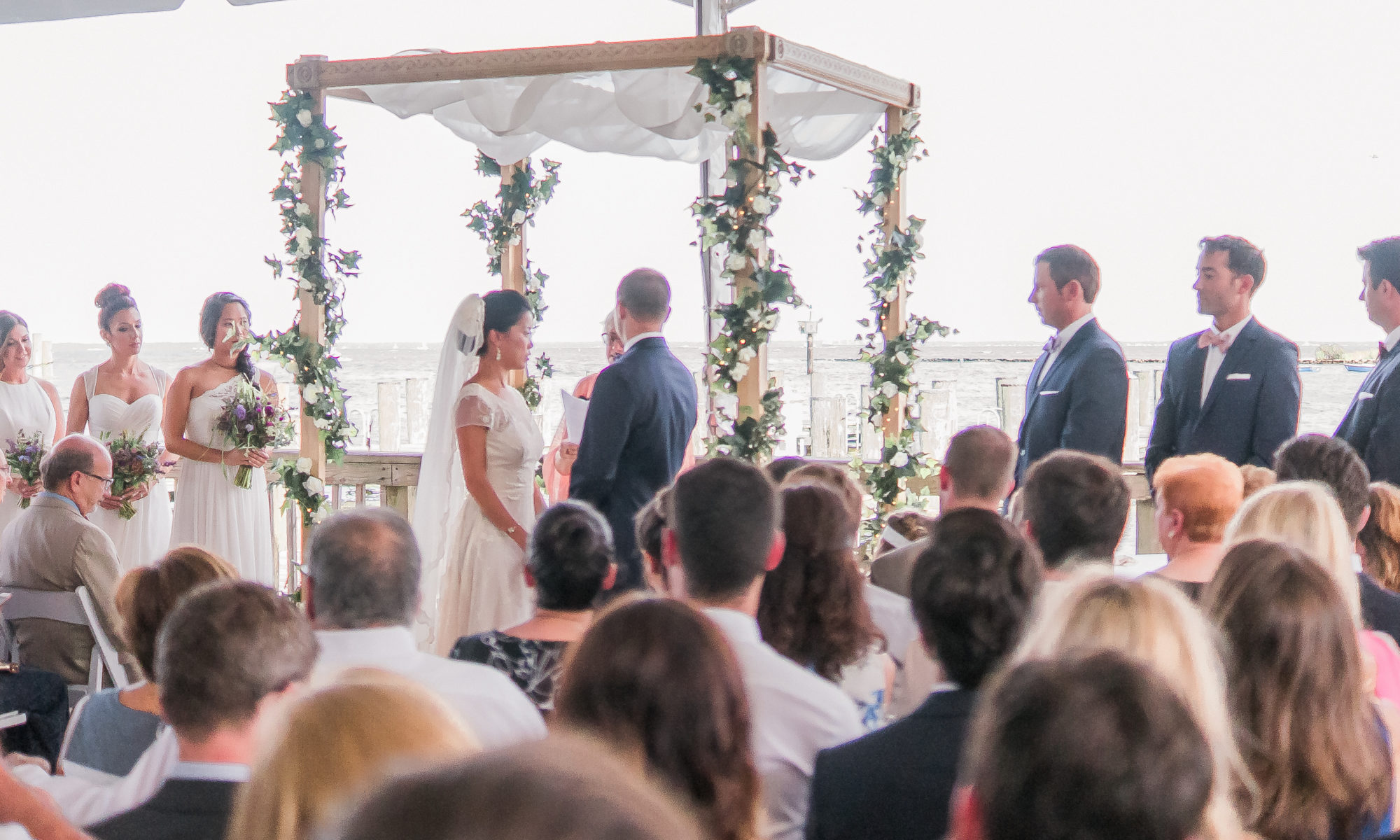 Outdoor waterfront wedding ceremony under a floral arch