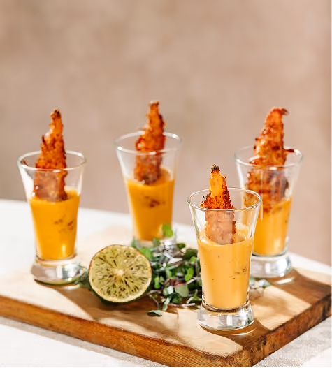 Soup shooters with crispy garnishes on a wooden board