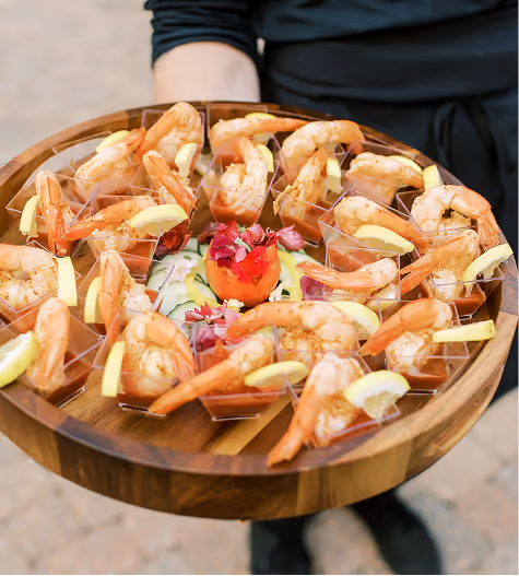 Server holding a wooden platter of shrimp cocktail