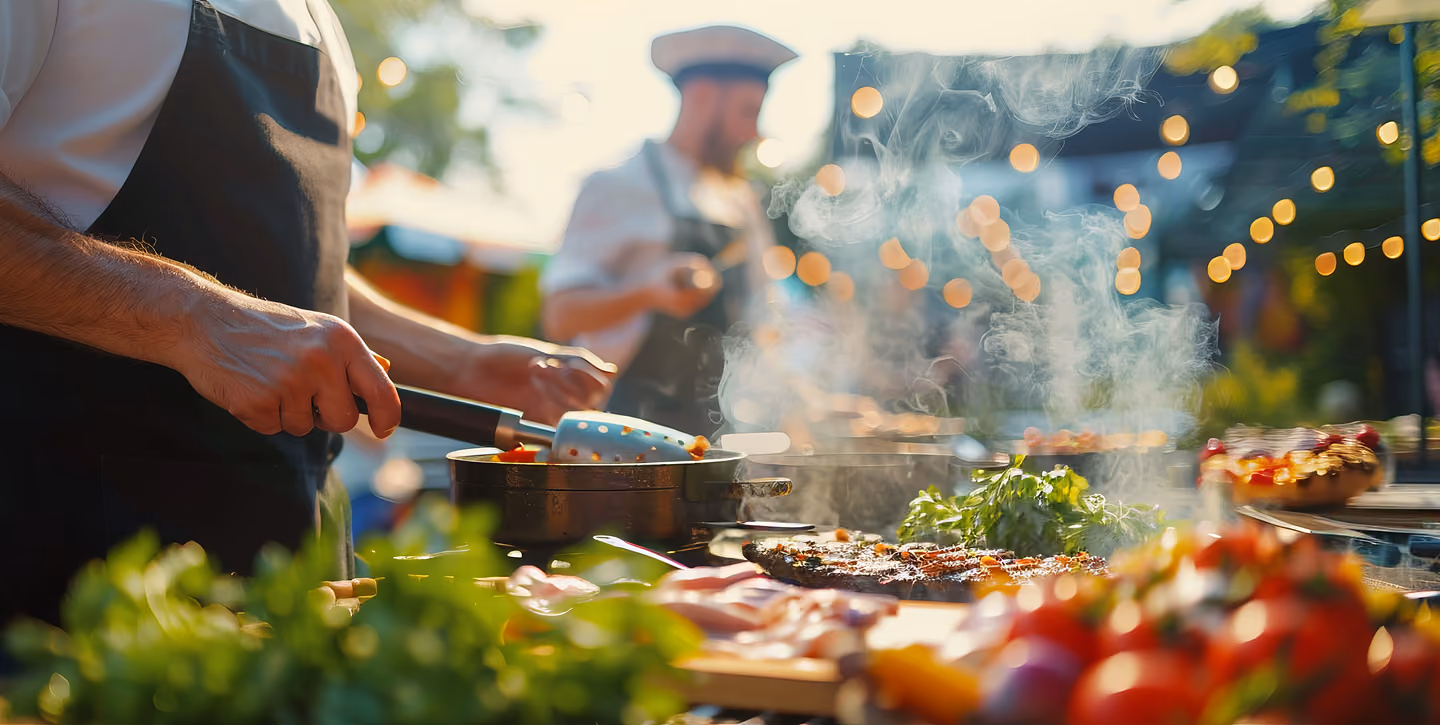Chef grilling meat and vegetables outdoors at a catered event