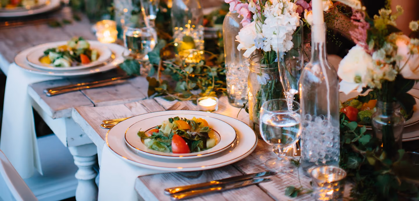 Long dinner table set with plated salads, candles and flowers