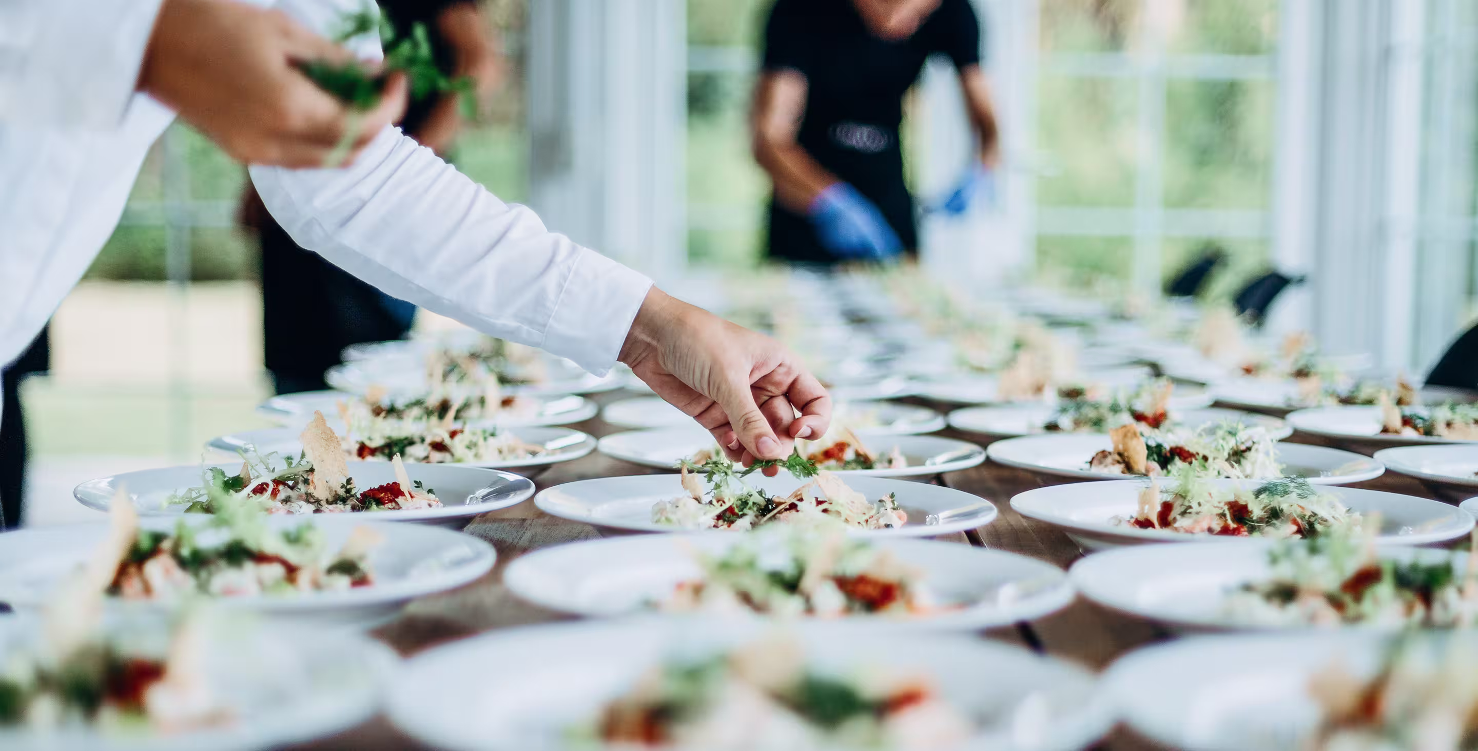 Server garnishing rows of plated salads before dinner service