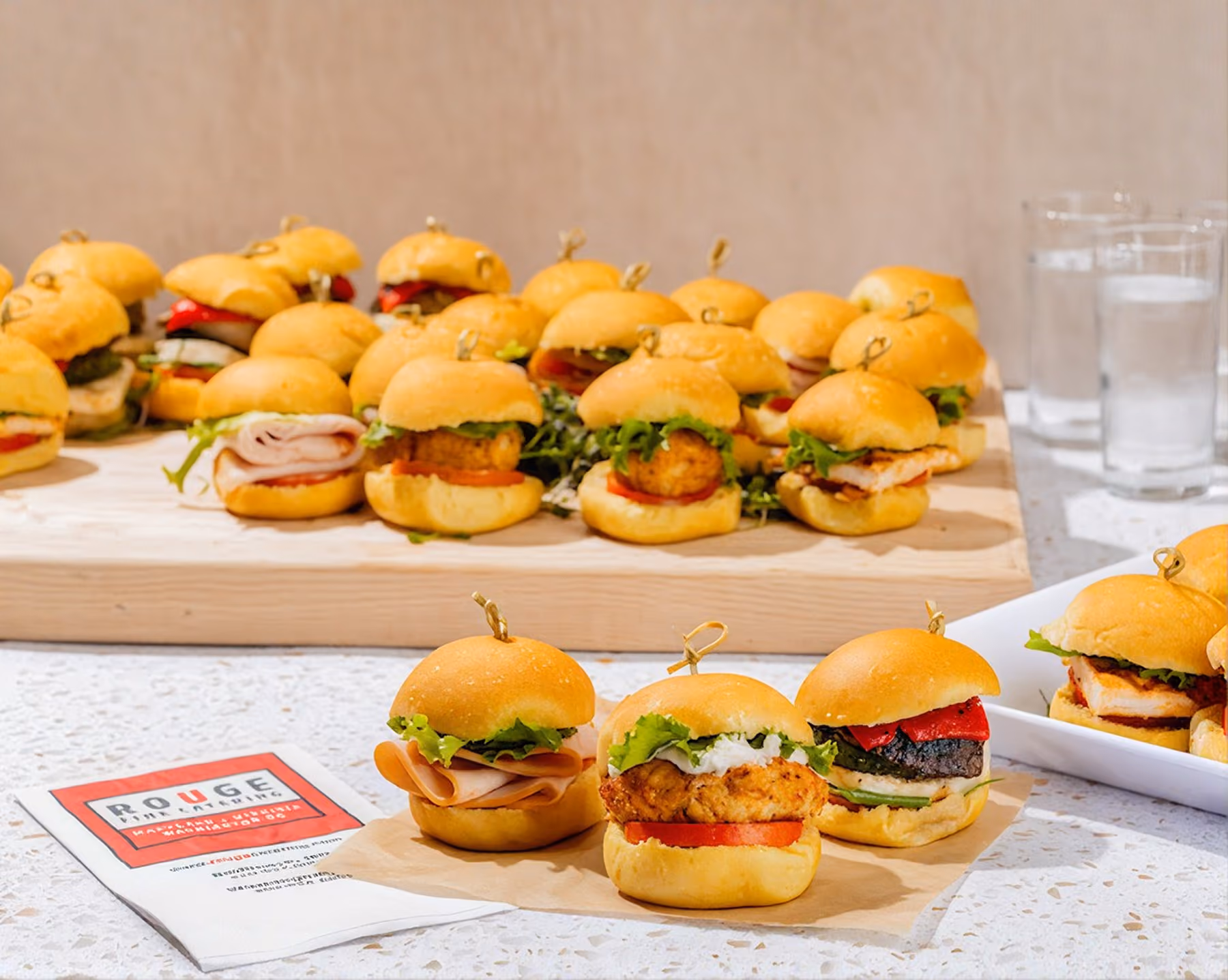 Slider sandwiches on wooden boards with a Rouge Catering card