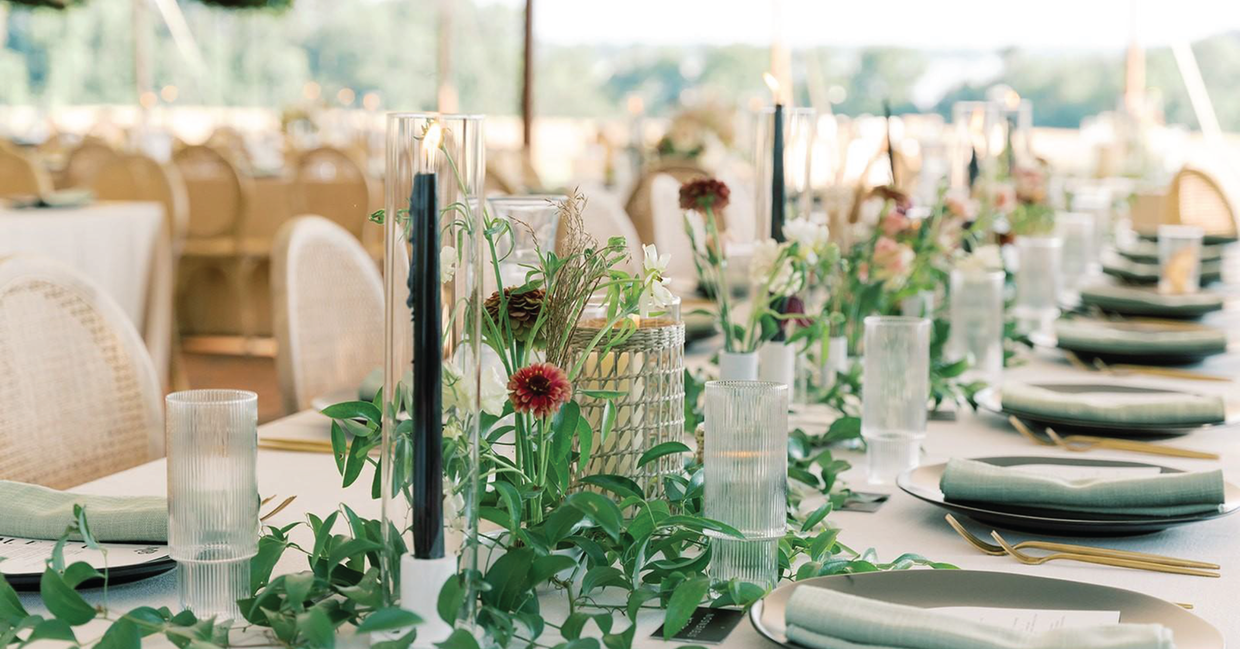 Long wedding reception tables set with greenery, candles and white place settings