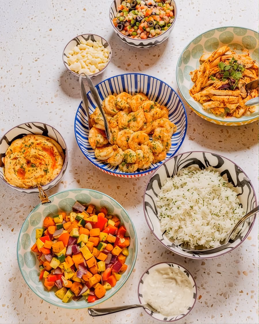 Drop-off catering spread of shrimp, roasted vegetables, rice and salads in serving bowls