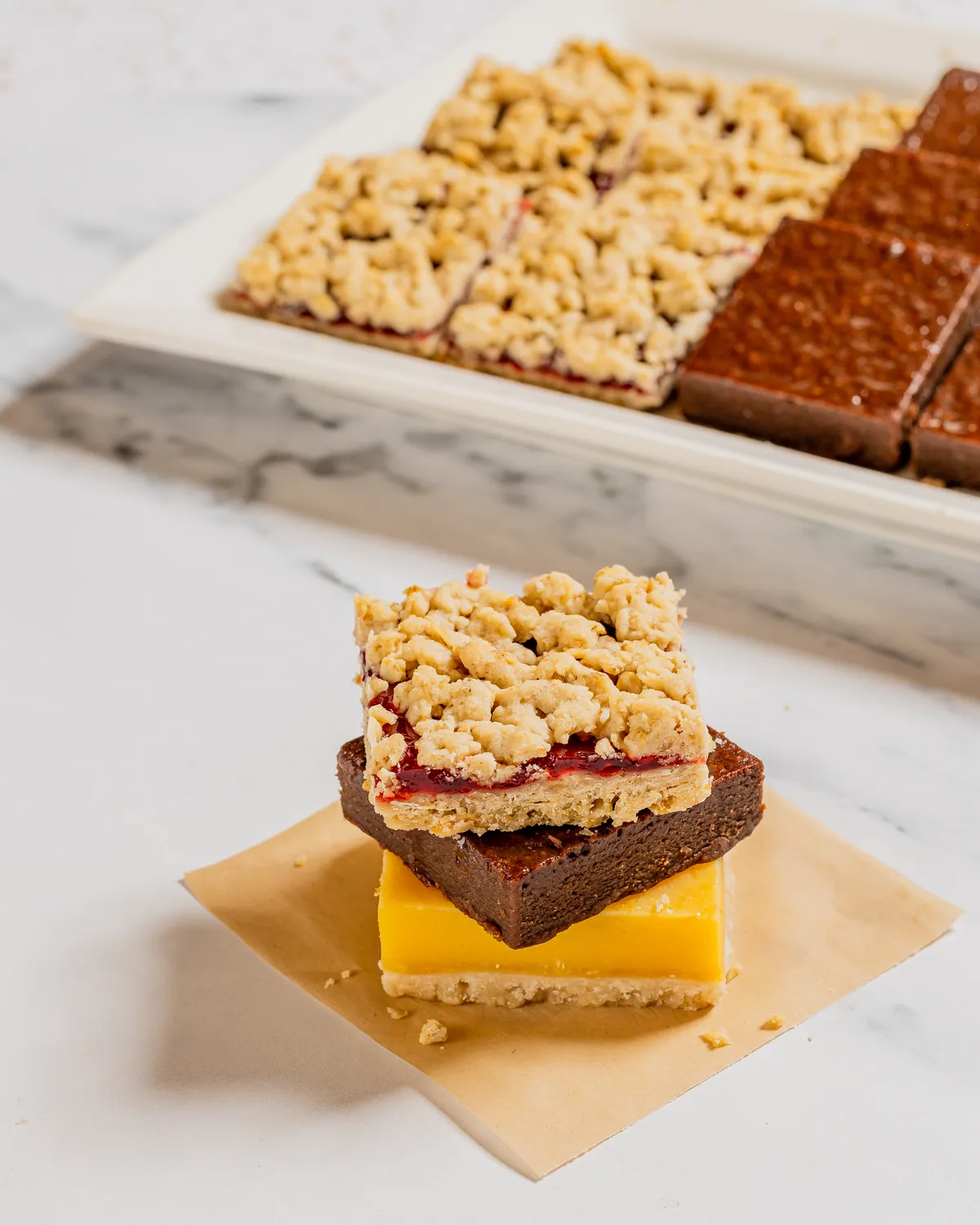 Stacked dessert bars, including brownies and lemon bars, on a marble counter
