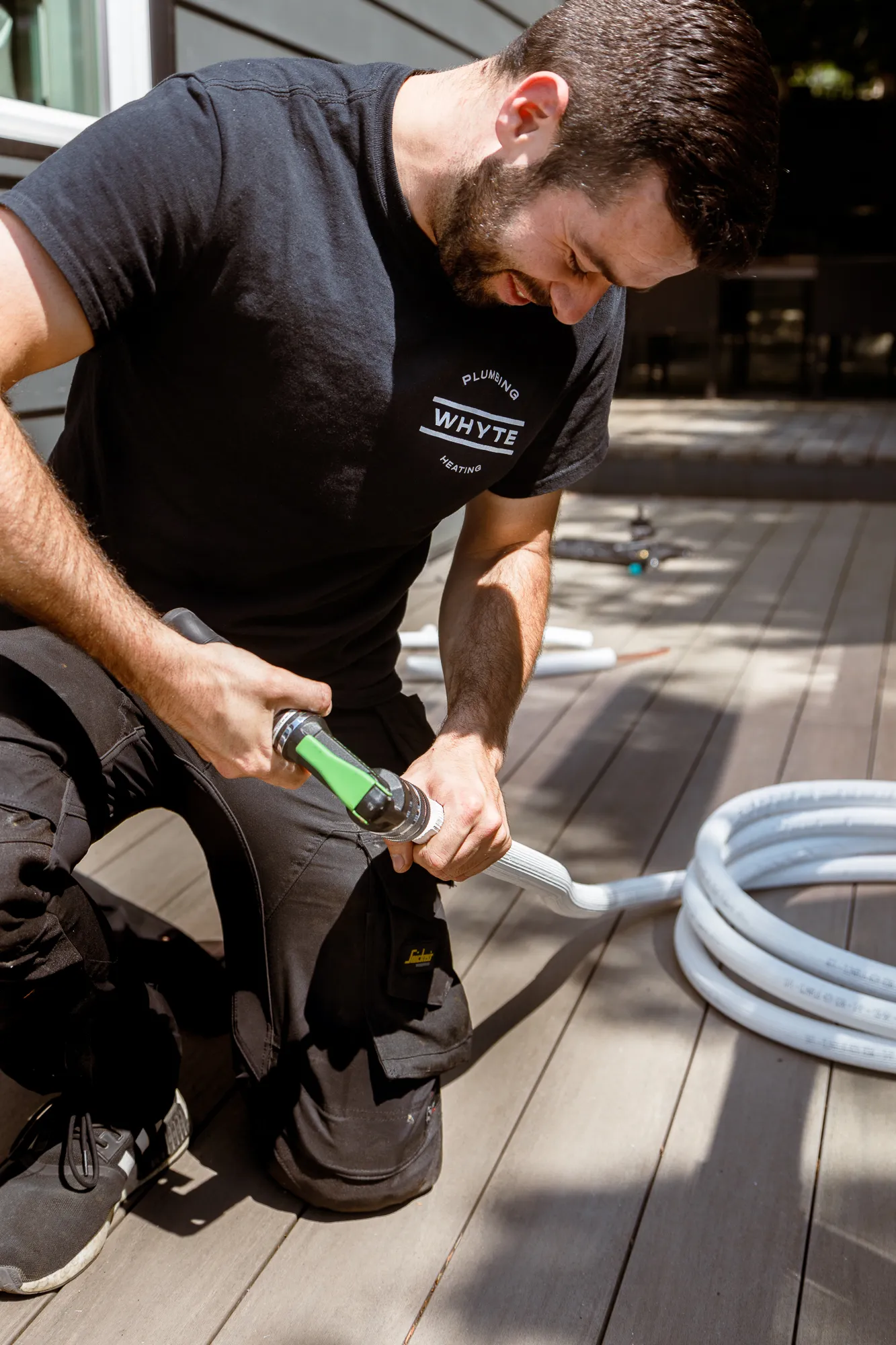 Whyte plumber kneeling on a deck working with pipe