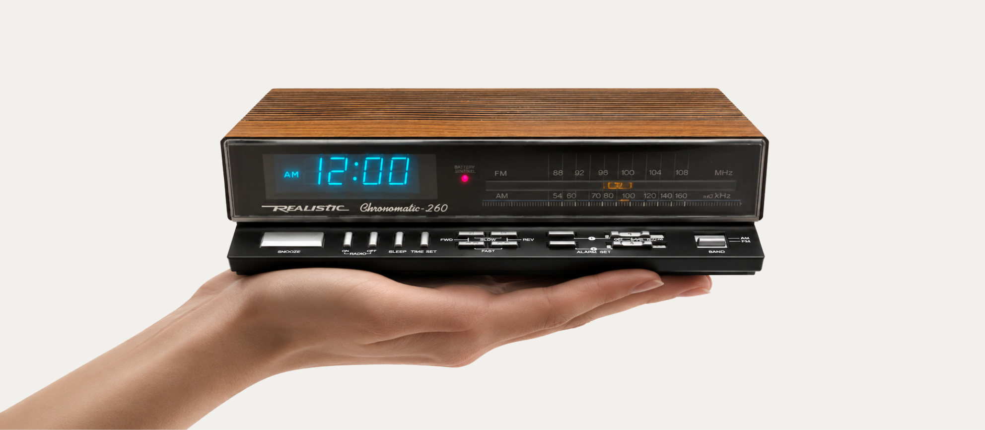A hand holding a Realistic Chronomatic-260 clock radio with a glowing blue display