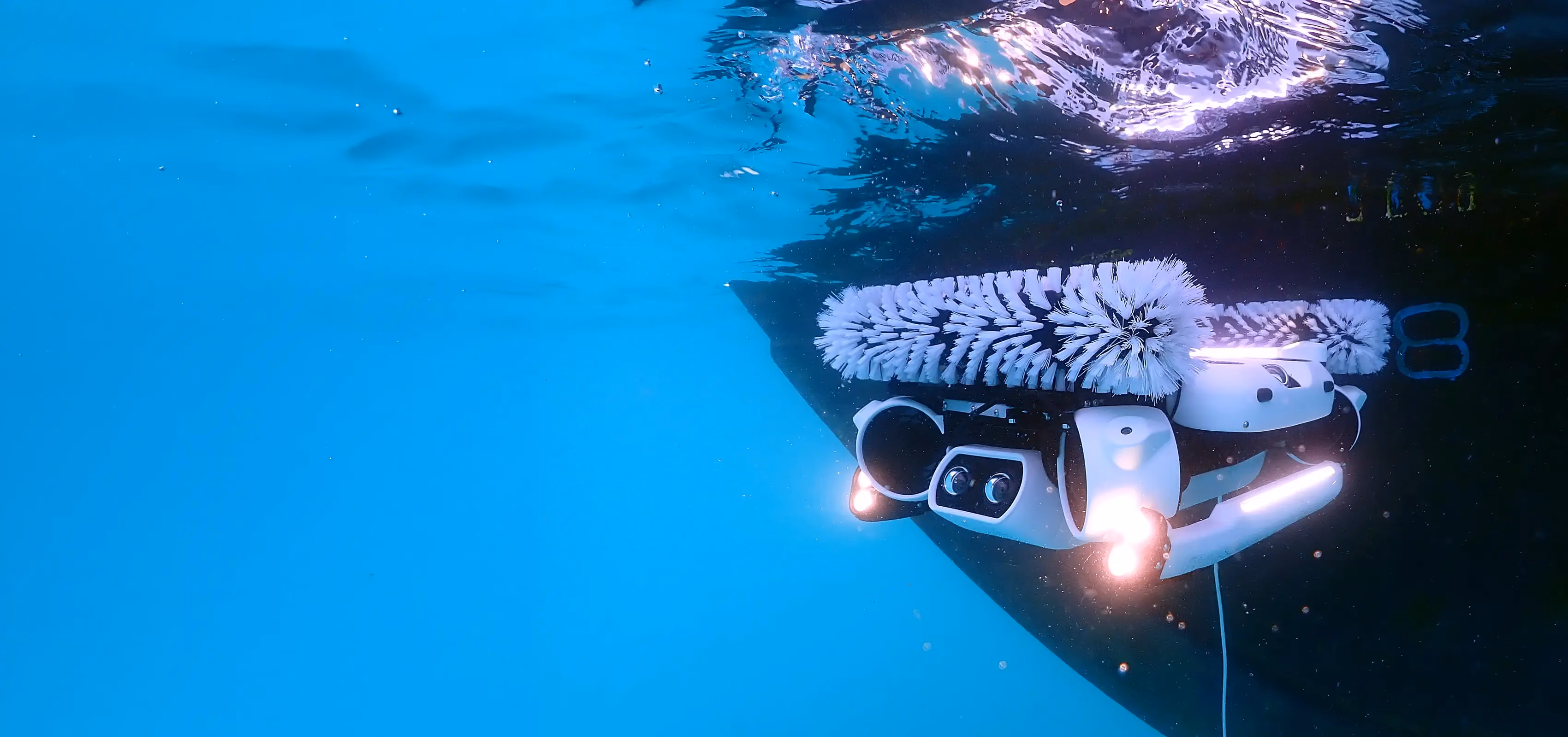 Hullbot robot with spinning brushes grooming the hull of a vessel in clear blue water