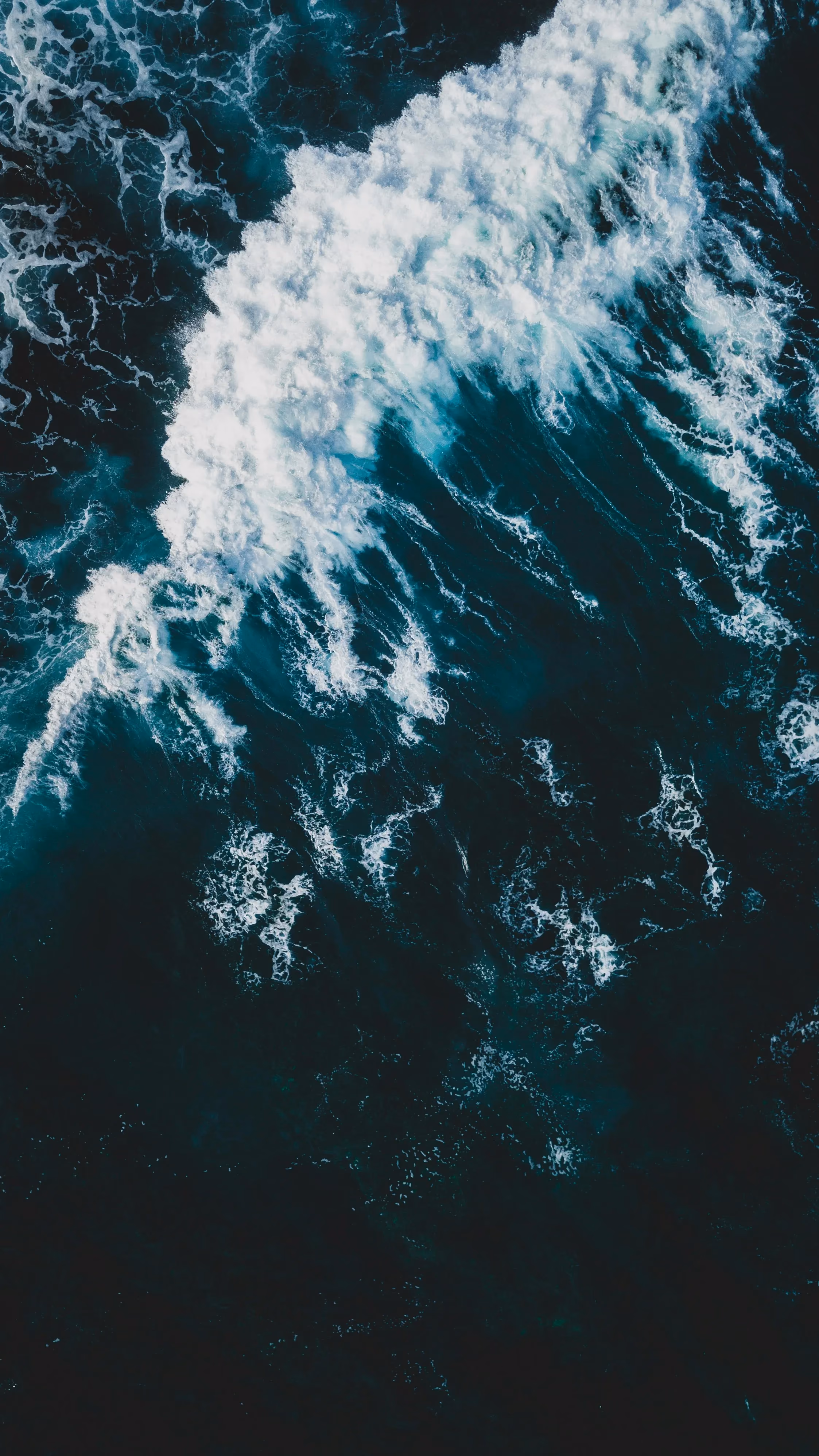 Aerial view of a dark ocean wave breaking into white foam