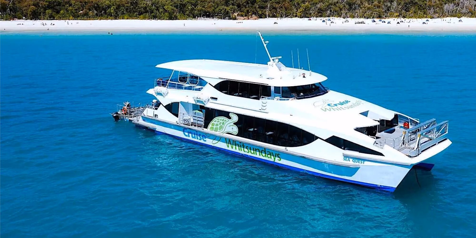 Cruise Whitsundays catamaran on turquoise water off a white sand beach