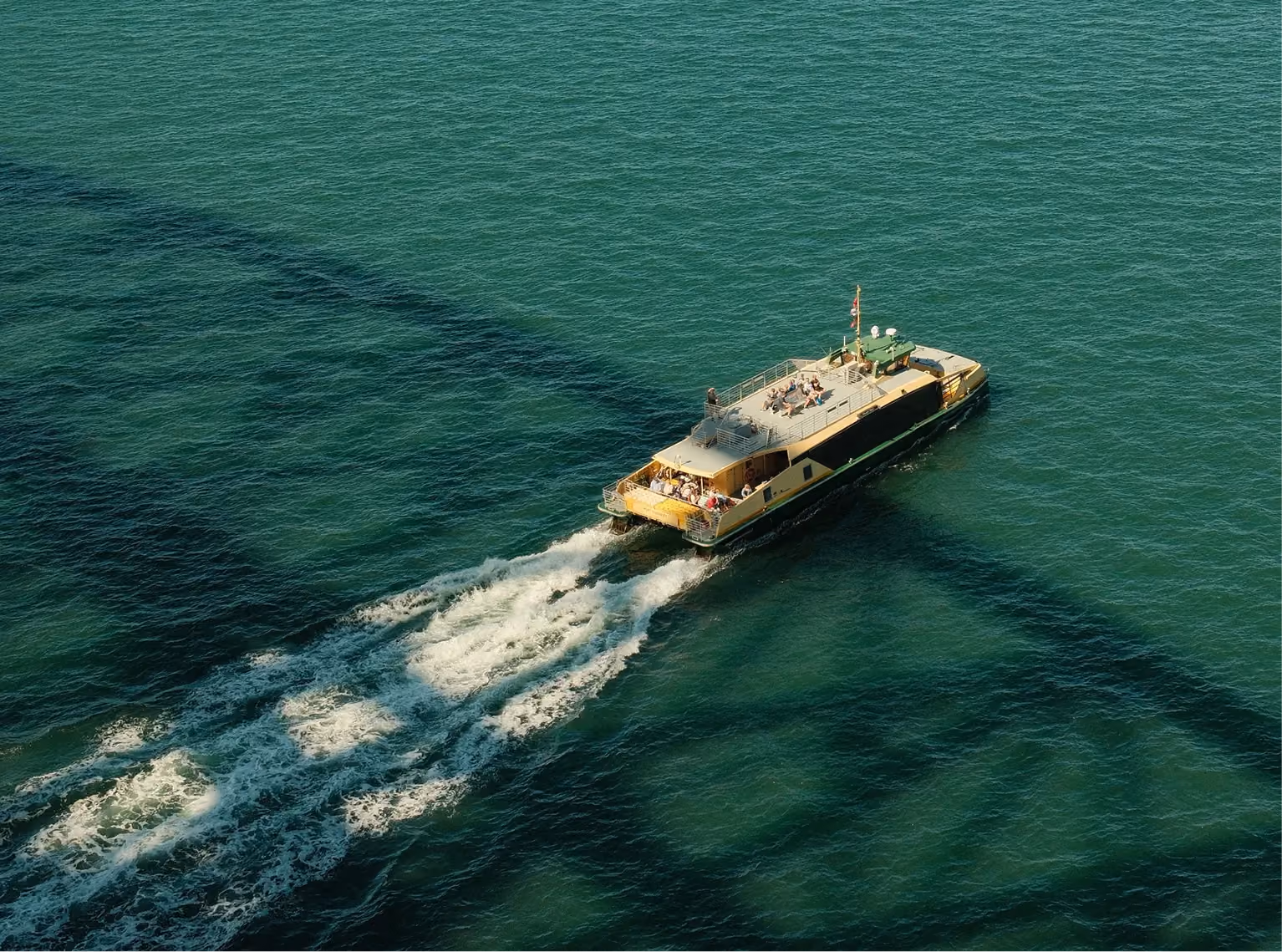 Aerial view of a harbour ferry leaving a white wake across green water
