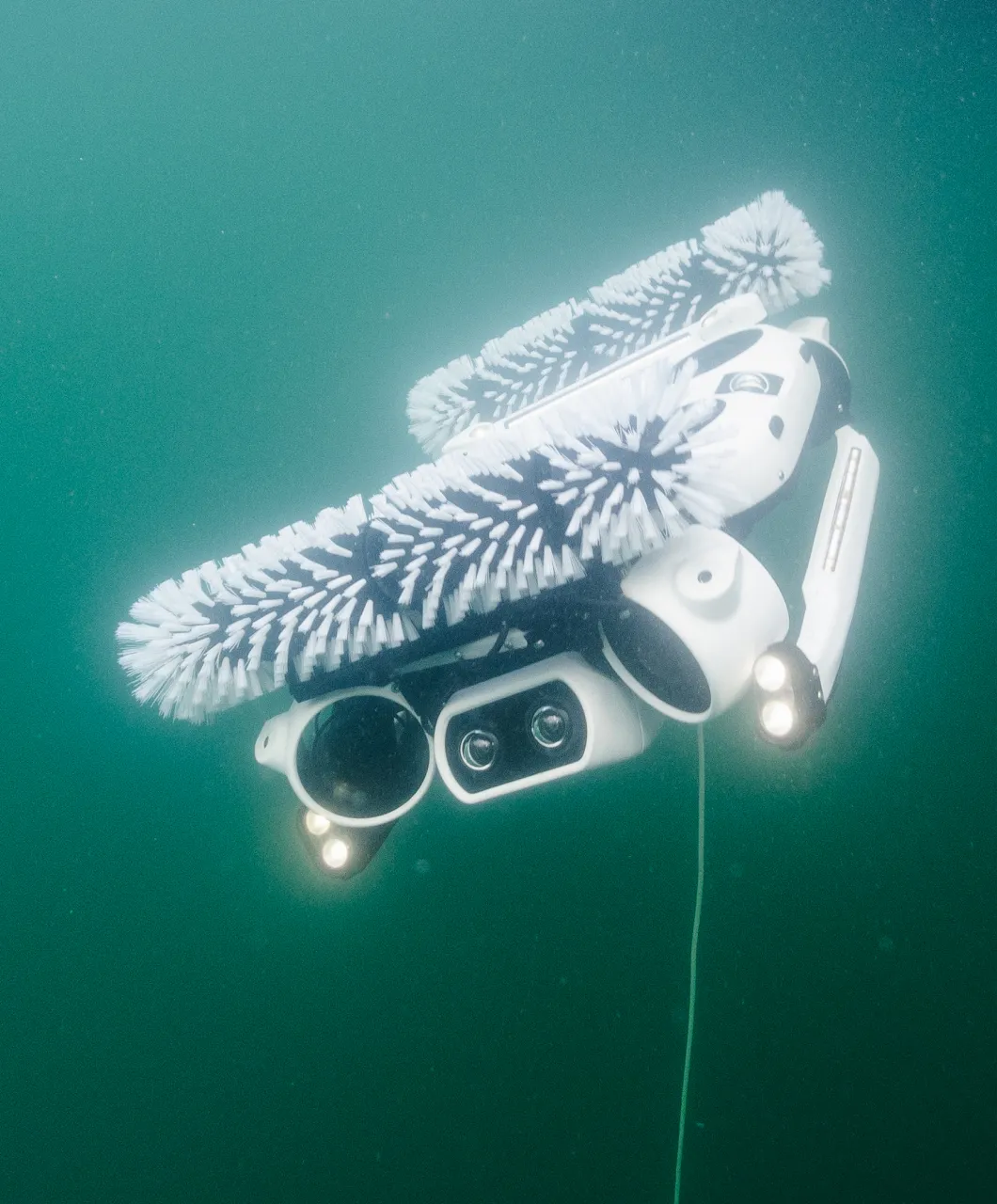 Hullbot robot with white rotating brushes and lights on, swimming through green water