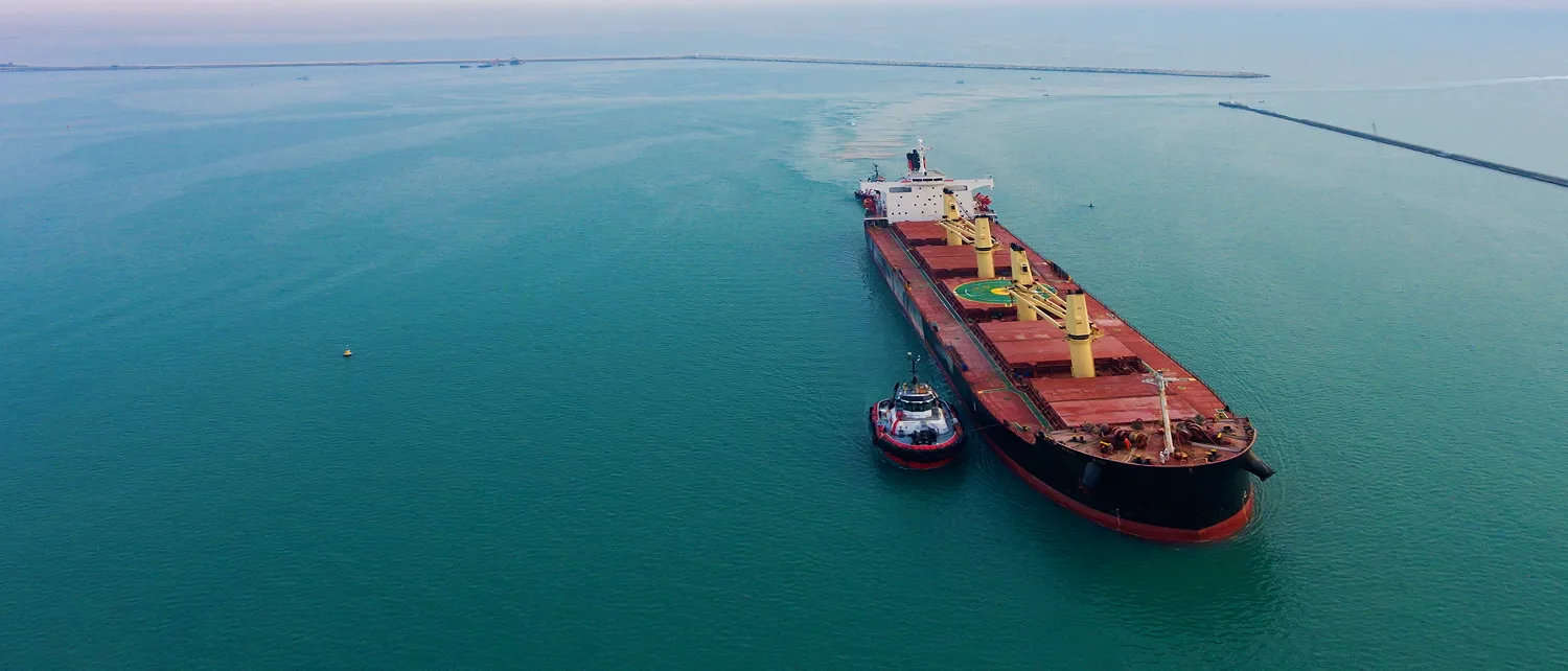 Aerial view of a bulk carrier with a tug alongside in calm green water