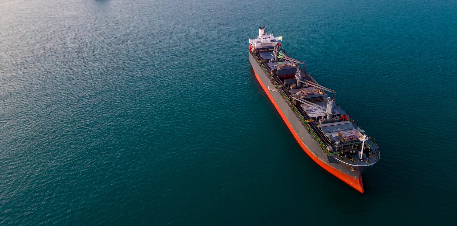 Aerial view of a bulk carrier with a red hull on calm green water