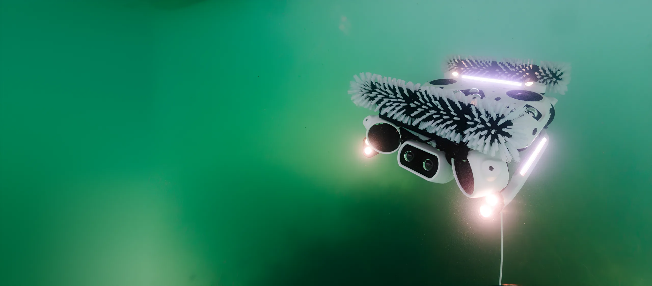 Hullbot robot with brushes and lights on, swimming through green water
