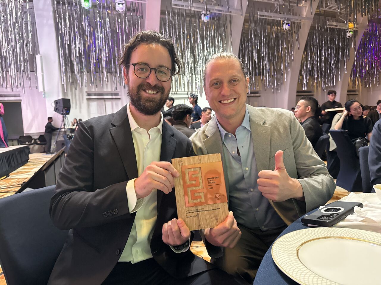 Two members of the Hullbot team holding the Singapore Design Award trophy at the awards ceremony