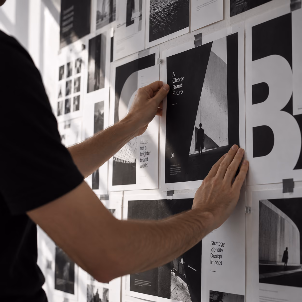 Iemand hangt zwart-wit posters op een muur, waaronder een met tekst 'A Clearer Brand Future' en silhouetten van personen tegen architecturale achtergronden.