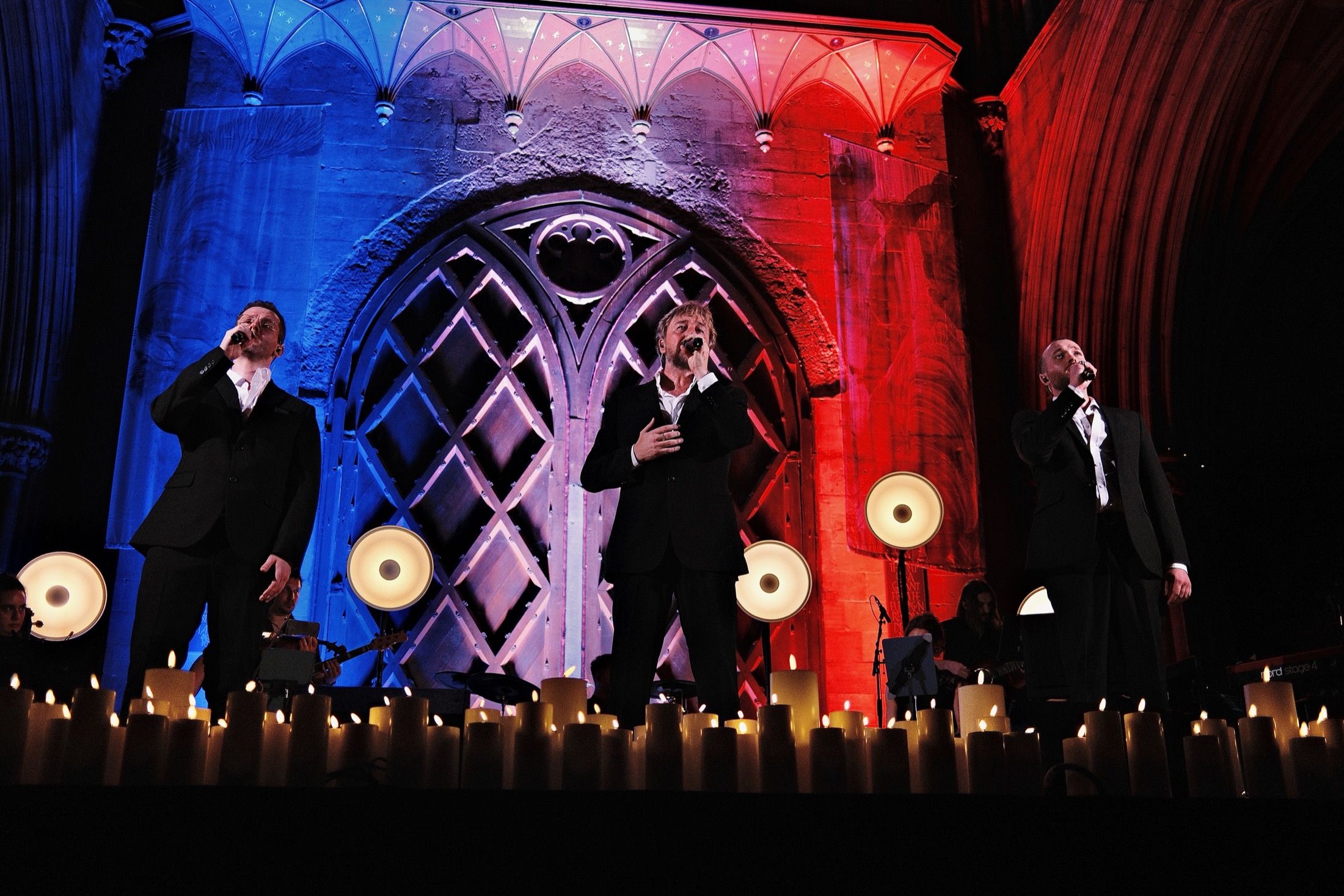 The three Valjeans singing in front of a lit cathedral window