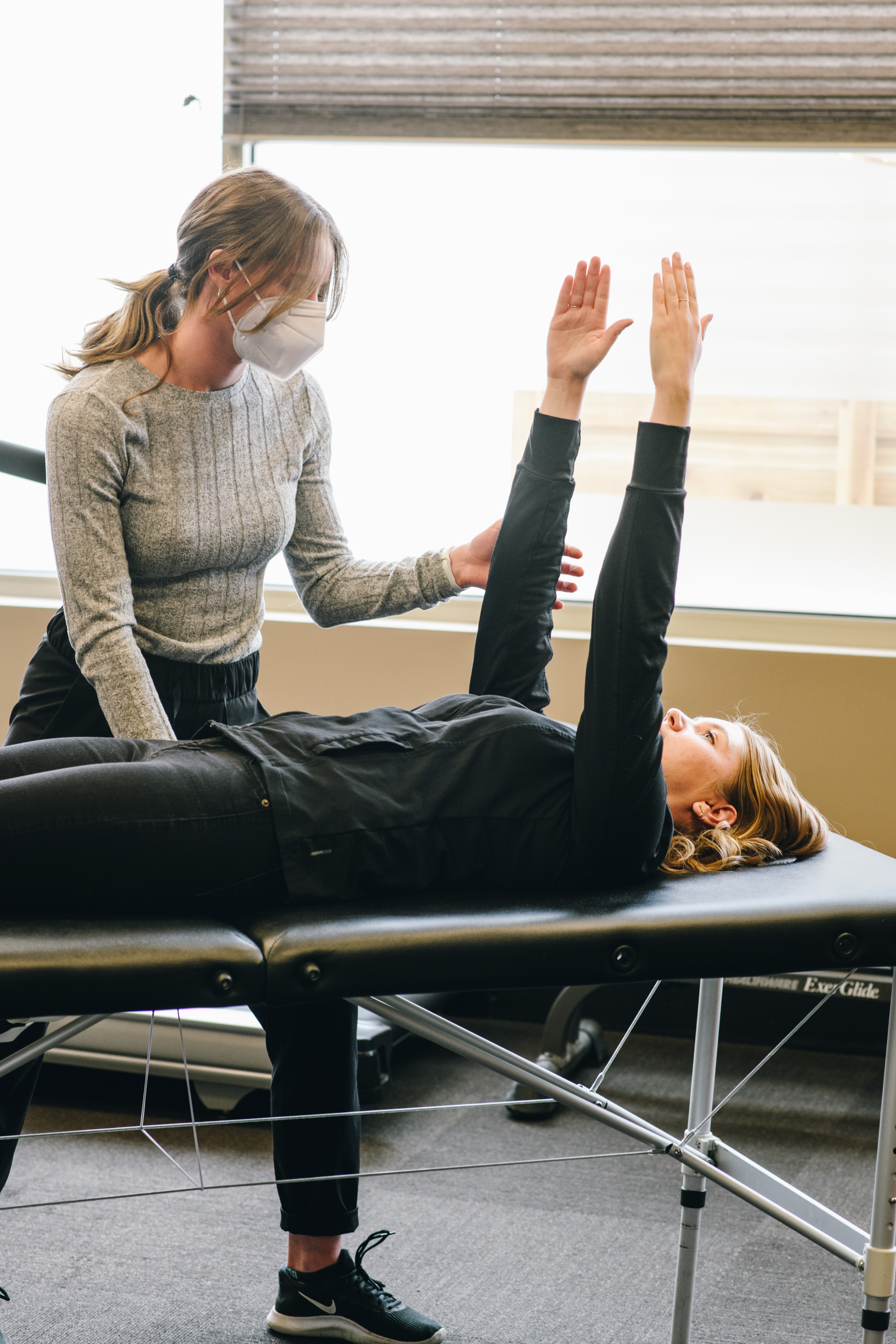 Clinician guiding a client through an overhead arm movement on a treatment table